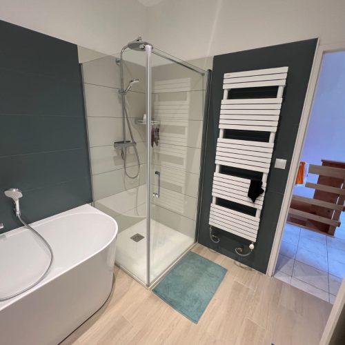 Salle de bain rénovée avec baignoire blanche, douche vitrée et sèche-serviettes mural