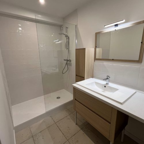 Salle de bain blanche avec douche vitrée et meuble vasque bois clair