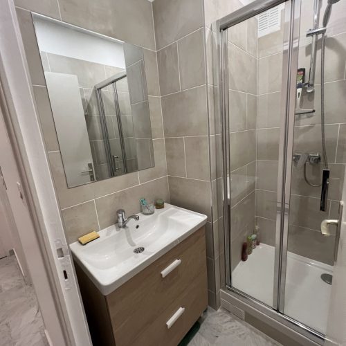 Salle de bain rénovée avec cabine de douche vitrée et meuble vasque en bois, carrelage beige