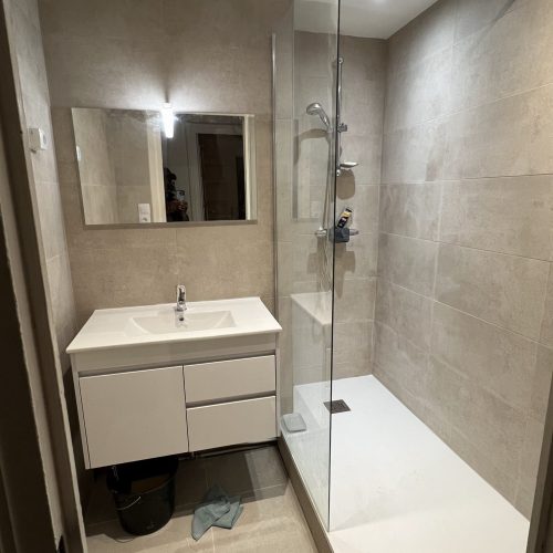 Salle de bain rénovée avec douche à l’italienne, meuble vasque suspendu et carrelage beige