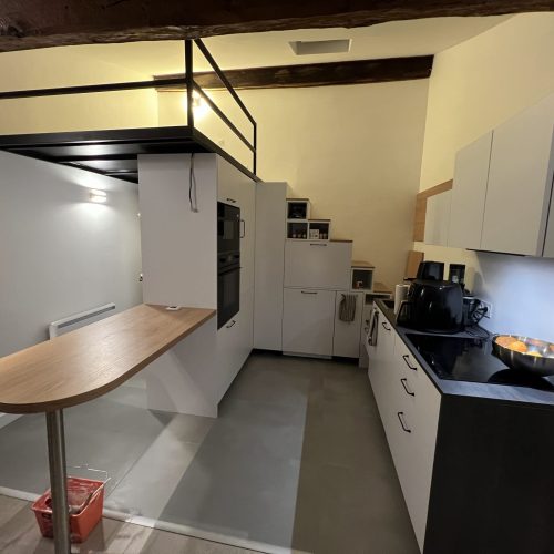 Rénovation complète d’un studio à Lyon avec mezzanine en métal noir, cuisine moderne blanche et plan de travail bois