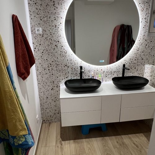 Salle de bain contemporaine avec meuble suspendu blanc, double vasque noire mate et miroir rond rétroéclairé